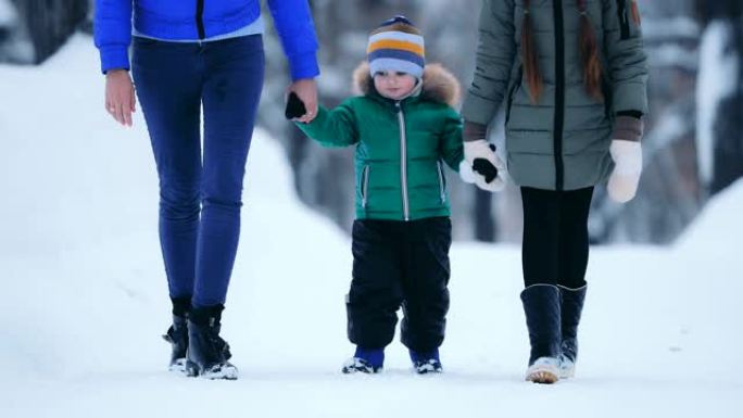 小男孩在冬天和他的母亲和妹妹一起走在路上。他们握着他的手，一起在冬季公园散步。