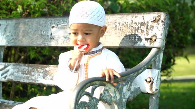 特写: 穆斯林儿子早上在公园的长凳上喜欢糖果
