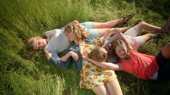 鸟瞰躺在田野里的女孩，他们互相挠痒痒，互相玩耍