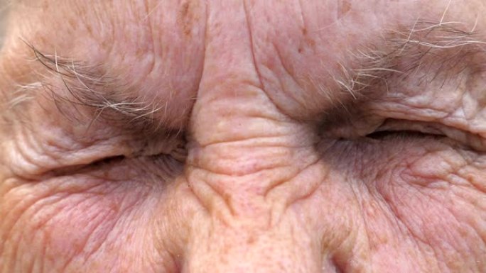 成熟女人的肖像拧起灰色的眼睛，然后睁开。老祖母皱着眉头的脸带着悲伤的目光看着镜头。高级女士的悲伤表情