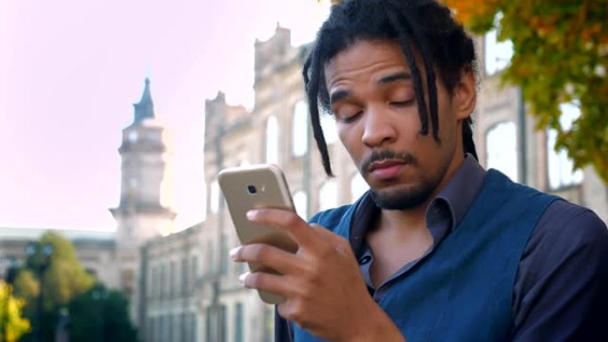 带有辫子的非裔美国学生的肖像，在大学背景下，在电话中观看内容，并在娱乐中观看内容。