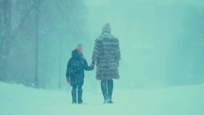 带着孩子的女人在冬天下大雪。他们穿着毛皮大衣和靴子。后视图。