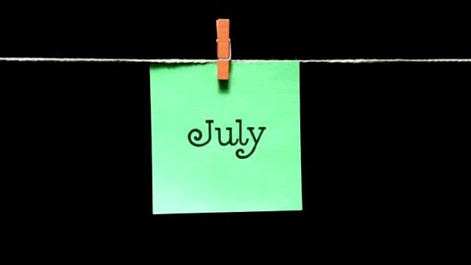 一年中的一个月。夏。在7月的铭文上。用绳子上的衣夹手动连接床单。黑色背景。