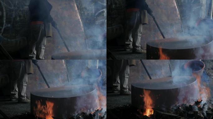男子在慢动作中与一个大铜锅一起在明火上工作