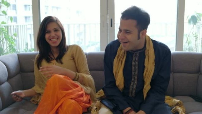 夫妻俩在电话视频会议上交谈时分享笑声和微笑，并穿着传统的印度服装与相机外的人交谈
