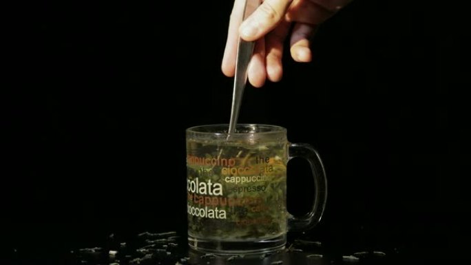 绿茶。将糖加入装有有机干绿茶和柠檬片的玻璃杯中，这些柠檬片漂浮在热水中。准备绿茶。慢动作。黑色背景