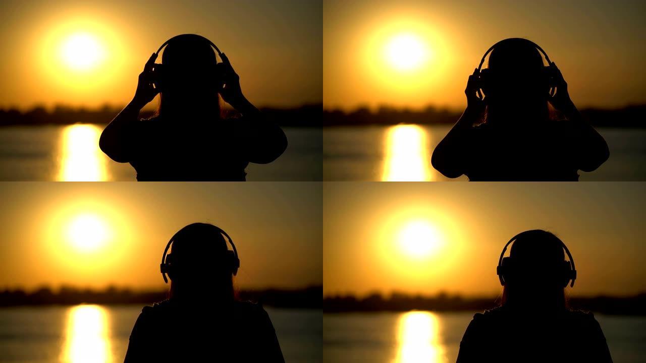 女人在日落背景上戴着耳机听音乐