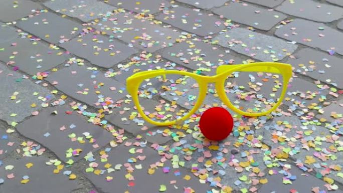 嘉年华-伪装眼镜，铺砌地面上的泡沫材料和彩色五彩纸屑的红色伪装鼻子-嘉年华概念或庆祝概念