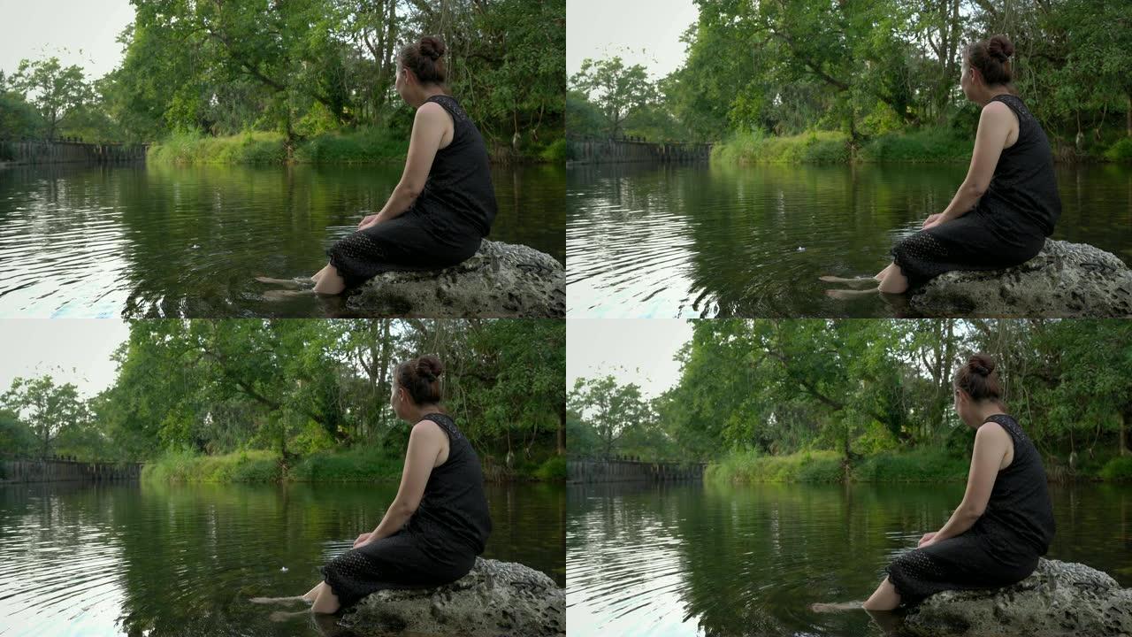 女人坐在溪流上的秋千上，在轻松的一天里，您的脚在水中缓慢而快乐地摆动。