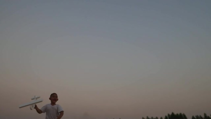 男孩在日落时在田野上奔跑的手中玩木制飞机