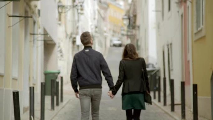 年轻夫妇在街上行走时手牵在一起的后视图。