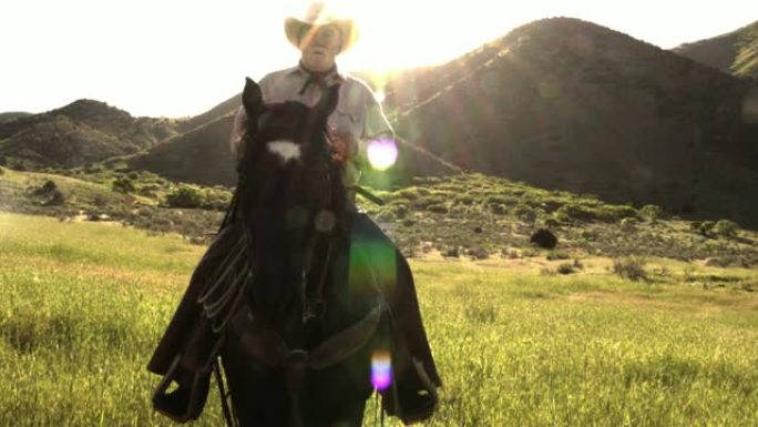 年迈的牛仔在山上骑着马，身后有一个旭日