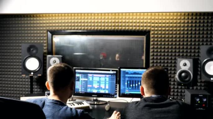 无法识别的年轻男性音频编辑和音乐制作人在录音棚工作。音响工程师在个人电脑上创作新歌。后视图特写慢动作