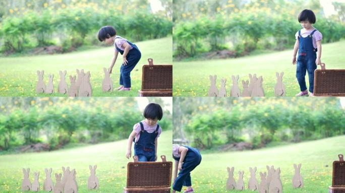 复活节那天可爱的小女孩。女孩在草坪上寻找复活节彩蛋，在大自然或公园和阳光下用纸制成的兔子。慢动作
