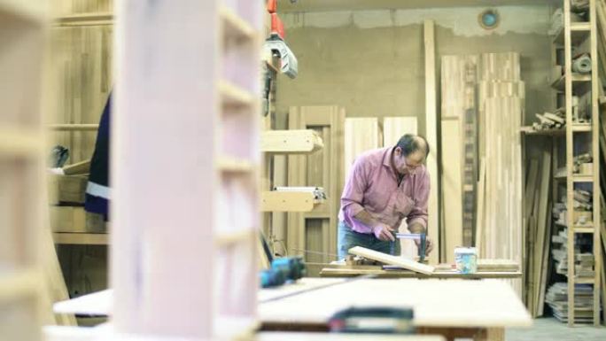 高级男子，体力劳动者-萨什曼 (sashman) 在小型家具工厂使用夹子将木制细节粘在一起。