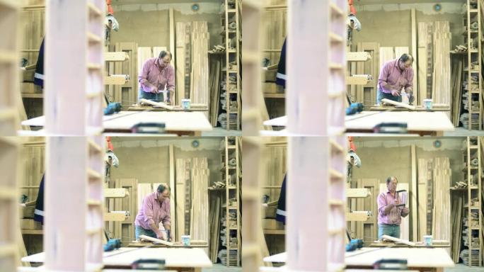高级男子，体力劳动者-萨什曼 (sashman) 在小型家具工厂使用夹子将木制细节粘在一起。