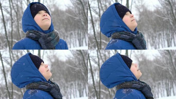 肖像年轻的十几岁的男孩在冬天的森林里享受雪，下雪