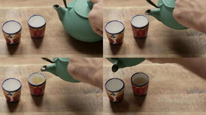 一只人手将热茶倒入两个带有茶箱的彩色杯子中