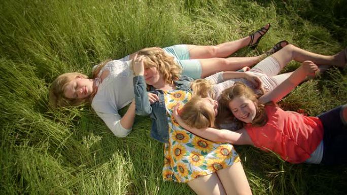 一组4个女孩躺在田野里，她们互相挠痒痒，玩草