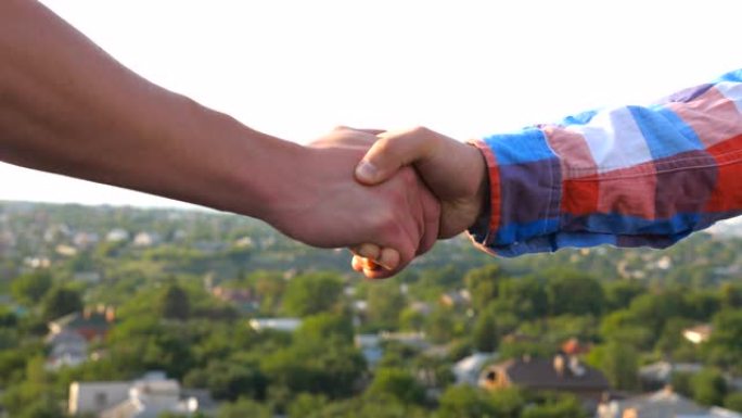 两个朋友在模糊的城市景观背景上握手。年轻人在屋顶上聚会并互相问候。户外男人之间友好的握手。友谊概念。