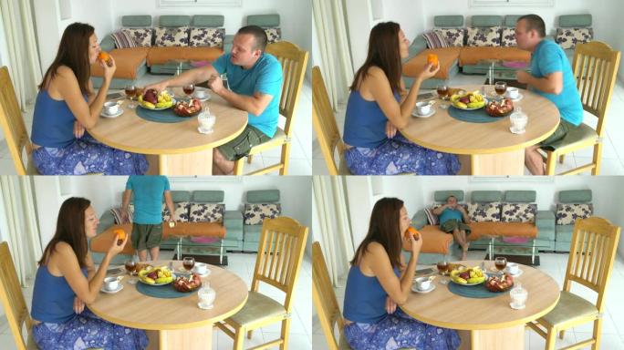 丈夫和妻子在家吃早餐。吃柿子的女人。一个男人拿了一个苹果