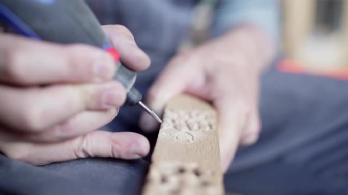 熟练木工的手使用电动雕刻工具在一块木头上进行雕刻装饰，特写
