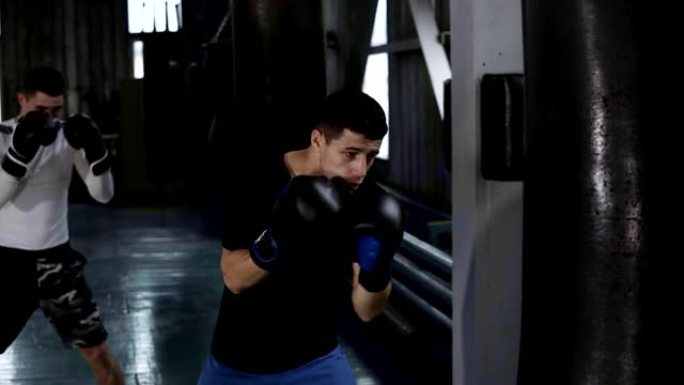 两名穿着便装的男拳击手正在殴打黑拳梨。努力，在拳击馆训练过程。侧视图