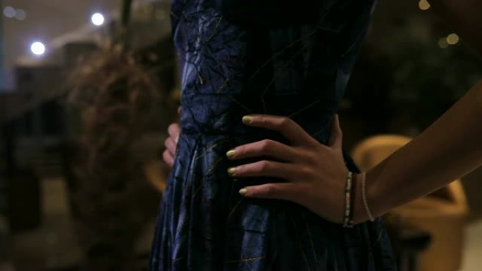 女士穿着优雅的蓝色连衣裙，双手放在臀部