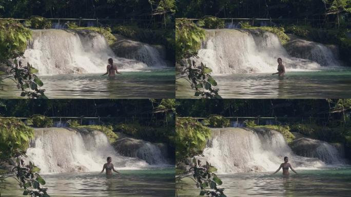 年轻女子沐浴在热带森林的瀑布中，水流溅到背景上。从丛林森林中的瀑布流淌在山河中的石头上。