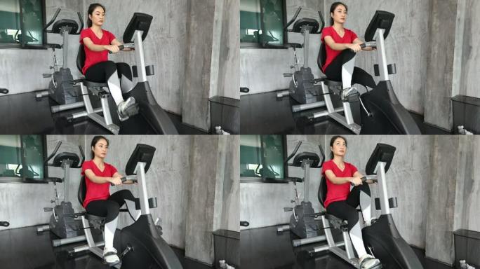 美女骑健身车骑自行车，在健身房用智能手机慢动作