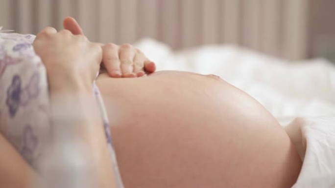 妇女的手将乳膏揉进她怀孕的肚子里，从分配器中挤出更多的乳膏，并不断地揉进皮肤里