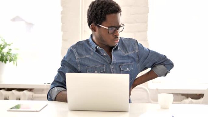 非洲男子背痛在笔记本电脑上工作