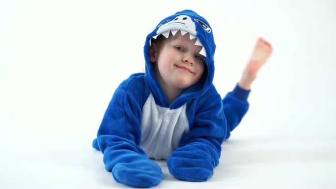 穿着睡衣kigurumi，蓝鲨服装在白色背景上摆姿势的开朗小男孩