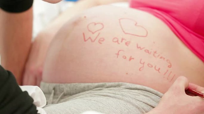 特写: 男人在怀孕的肚子上写字