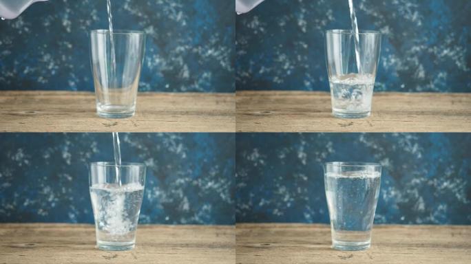 男人的手慢慢地把新鲜干净的水从水罐里倒进玻璃杯里。木制桌子和蓝色背景上的玻璃烧杯。活水，健康饮料
