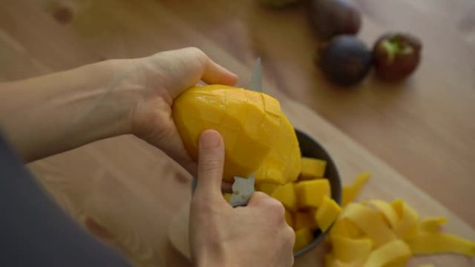一名年轻女子将芒果切成立方体的4倍慢动作镜头，桌子上放着许多热带水果