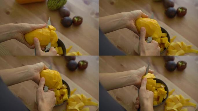 一名年轻女子将芒果切成立方体的4倍慢动作镜头，桌子上放着许多热带水果
