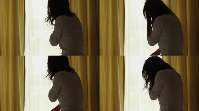 一个年轻悲伤的女人坐在窗户附近的剪影