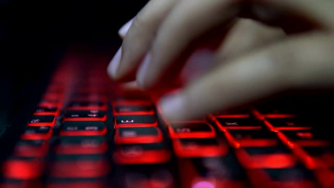 十几岁的黑客女孩在黑暗中攻击公司服务器，在红色照明的笔记本电脑键盘上打字。房间很暗