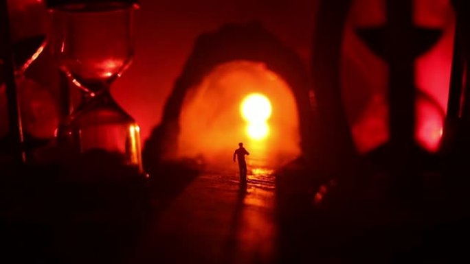 时间概念。一个男人站在沙漏之间的剪影，烟熏和黑暗背景上的灯光。超现实装饰图片