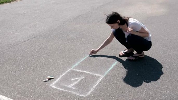 女人用五颜六色的粉笔在沥青上画跳房子。