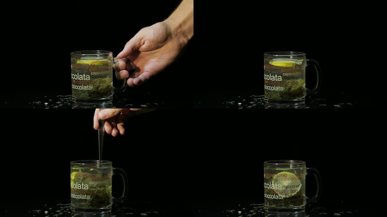 男人的手放了一个装有绿茶的玻璃杯。装有有机干绿茶和柠檬片的玻璃杯，漂浮在热水中的杯子内。慢动作。黑色