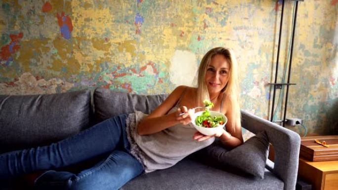 健康女人在沙发上吃新鲜沙拉