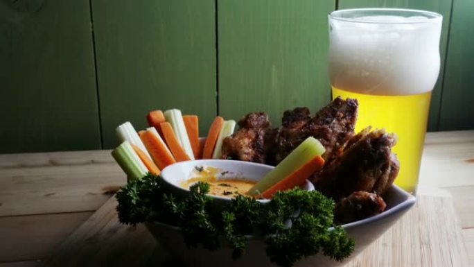 一碗健康的烤鸡翅，配以辣酱芹菜和胡萝卜条，配以啤酒