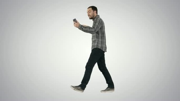 蓄着胡须的英俊男子一边用智能手机记录视频博客，一边在渐变背景上行走