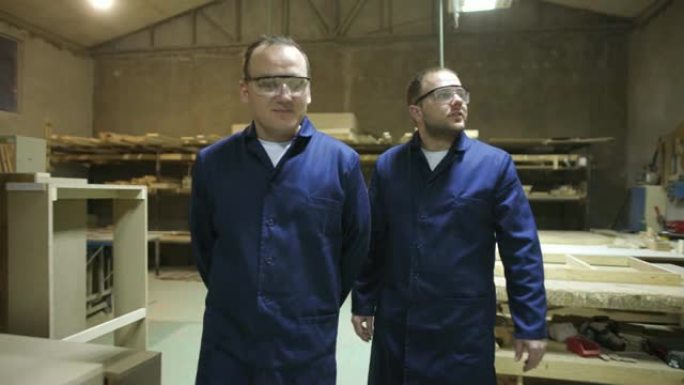 两名戴着安全镜的工人在家具工厂里走路和说话