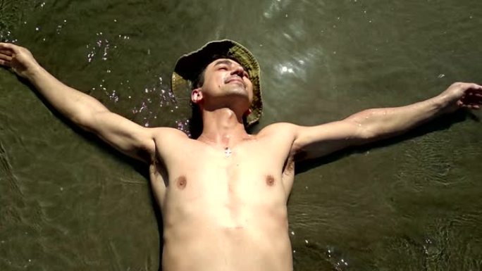 男人放松在阳光下躺在沙滩上的水中，度假的概念