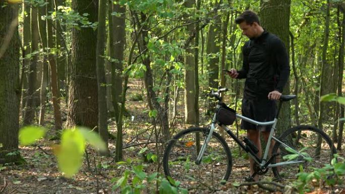 骑自行车的人站在森林里骑自行车，用智能手机工作