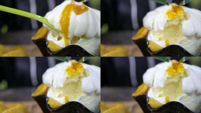 长绿勺子在芒果冰苏上舀白甜奶油的特写镜头。韩国冰甜点，由牛奶剃须冰制成，带有甜奶油，加切芒果和芒果酱