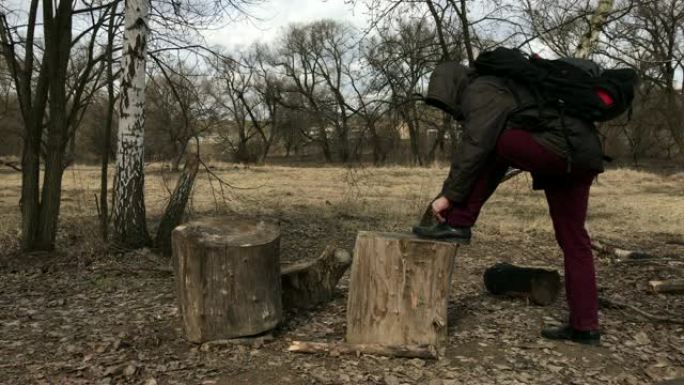 一个穿着外套的男人在春天的公园里散步。靠在木制甲板上，拉直鞋子，然后走得更远。春天的风景。
